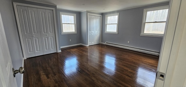 unfurnished bedroom featuring baseboard heating, dark wood-type flooring, crown molding, and multiple closets