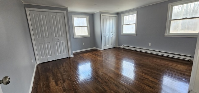 unfurnished bedroom featuring baseboard heating, dark hardwood / wood-style flooring, ornamental molding, and multiple closets