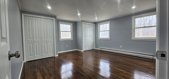 unfurnished bedroom featuring a baseboard heating unit, multiple closets, crown molding, and dark hardwood / wood-style floors