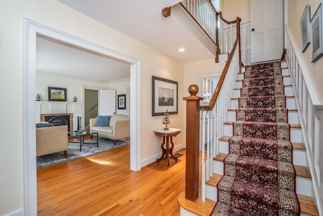 stairs with a fireplace, hardwood / wood-style floors, and crown molding