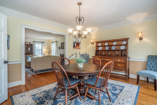 dining space with light wood-type flooring, crown molding, and an inviting chandelier