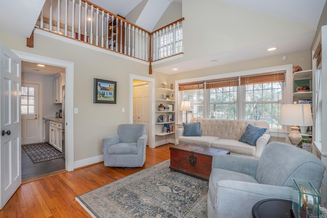 living room with built in shelves, light wood-type flooring, high vaulted ceiling, and plenty of natural light