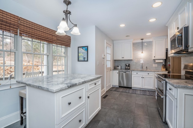 kitchen with light stone countertops, appliances with stainless steel finishes, backsplash, decorative light fixtures, and white cabinets