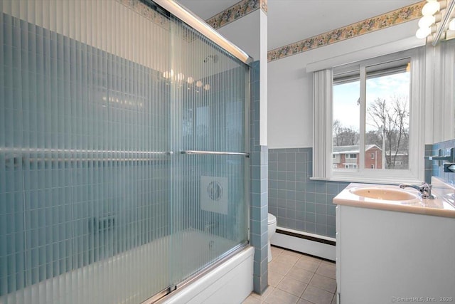 full bathroom featuring vanity, a baseboard heating unit, tile patterned floors, bath / shower combo with glass door, and tile walls