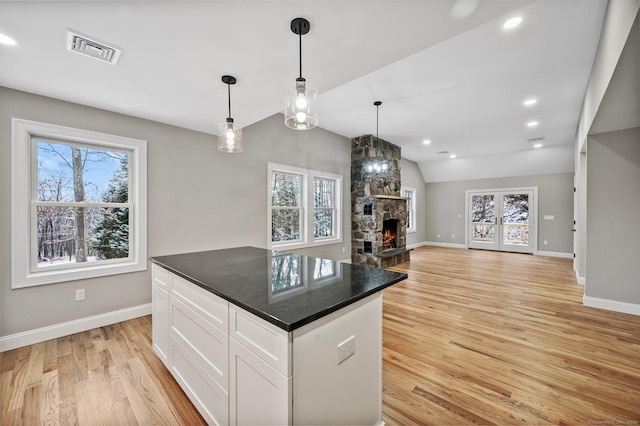 kitchen featuring pendant lighting, white cabinetry, dark stone counters, a fireplace, and light hardwood / wood-style flooring