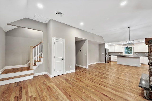 unfurnished living room featuring light wood-type flooring, lofted ceiling, and sink