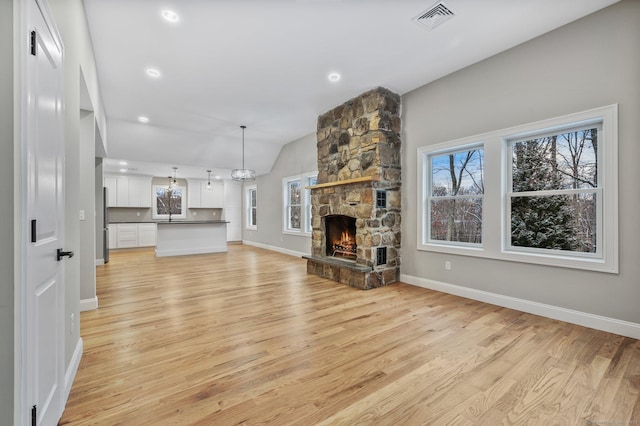 unfurnished living room with light hardwood / wood-style floors, a stone fireplace, and vaulted ceiling