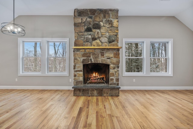 unfurnished living room with an inviting chandelier, lofted ceiling, a stone fireplace, and a healthy amount of sunlight