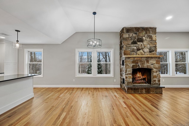 unfurnished living room featuring vaulted ceiling, an inviting chandelier, a fireplace, and light hardwood / wood-style flooring