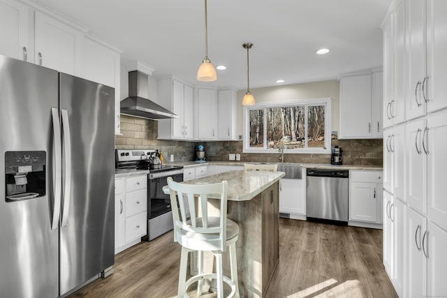 kitchen with a kitchen island, pendant lighting, white cabinetry, appliances with stainless steel finishes, and wall chimney exhaust hood