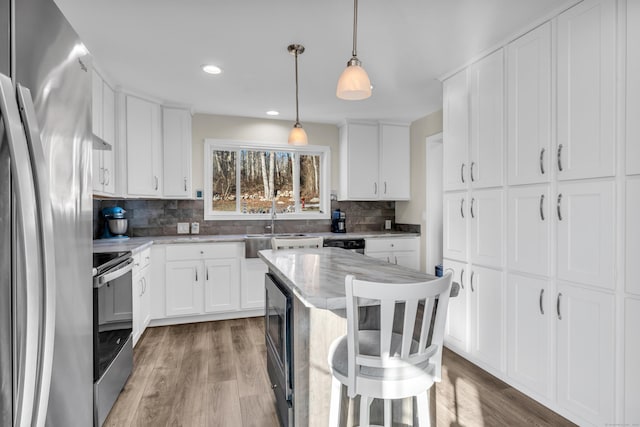 kitchen featuring decorative backsplash, white cabinets, hanging light fixtures, and appliances with stainless steel finishes