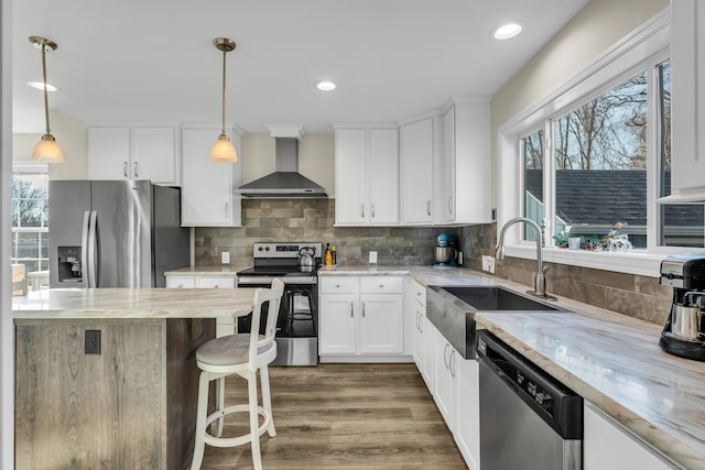 kitchen featuring white cabinets, wall chimney exhaust hood, stainless steel appliances, sink, and light stone counters