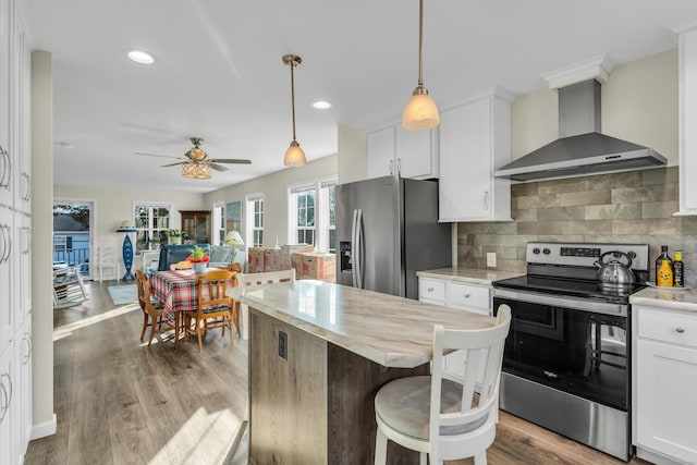 kitchen with a center island, wall chimney exhaust hood, white cabinetry, stainless steel appliances, and tasteful backsplash