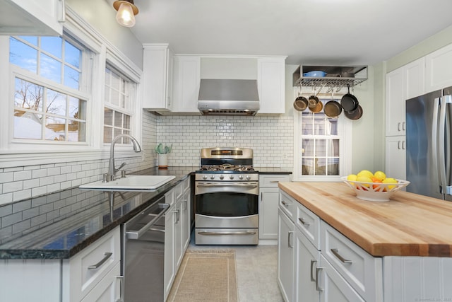 kitchen featuring sink, wall chimney exhaust hood, stainless steel appliances, butcher block countertops, and white cabinets