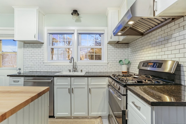 kitchen with exhaust hood, sink, butcher block countertops, white cabinetry, and stainless steel appliances