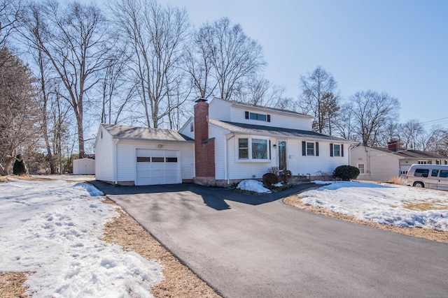 view of front of property featuring aphalt driveway, an attached garage, a storage shed, a shingled roof, and a chimney