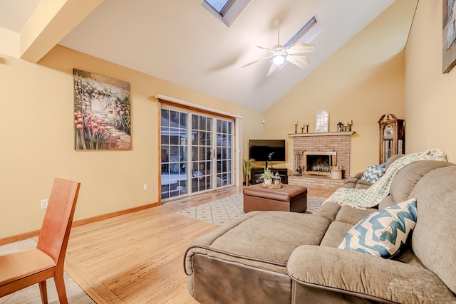 living room featuring high vaulted ceiling, a brick fireplace, ceiling fan, a skylight, and hardwood / wood-style floors