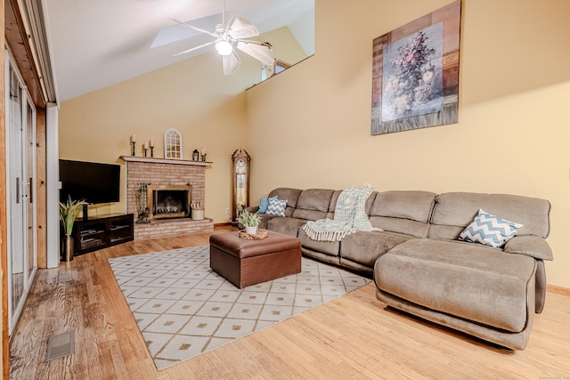 living room featuring light hardwood / wood-style floors, a brick fireplace, ceiling fan, and high vaulted ceiling