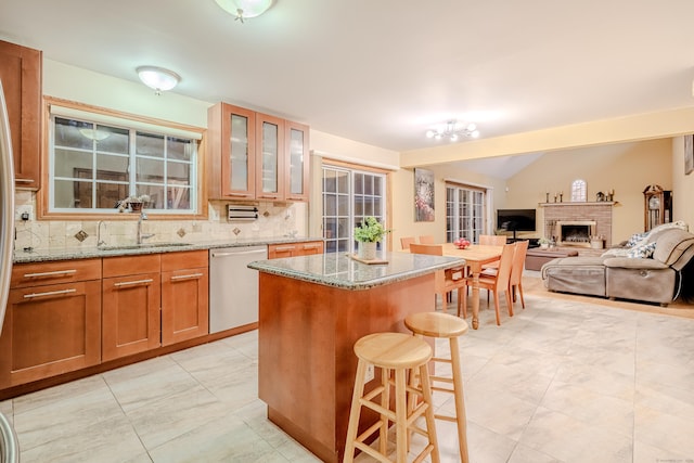 kitchen with lofted ceiling, sink, a center island, stainless steel dishwasher, and light stone countertops