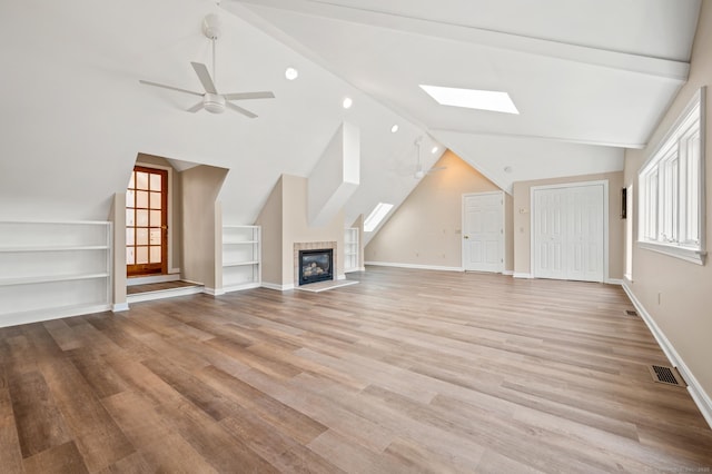 unfurnished living room featuring vaulted ceiling with skylight, a fireplace, light hardwood / wood-style floors, built in features, and ceiling fan