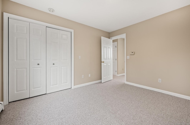 unfurnished bedroom featuring light carpet, a closet, and a baseboard heating unit