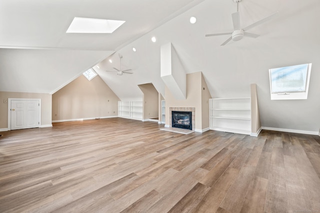 additional living space featuring vaulted ceiling with skylight, a fireplace, built in features, light wood-type flooring, and ceiling fan