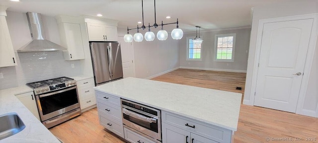 kitchen with wall chimney exhaust hood, hanging light fixtures, tasteful backsplash, white cabinets, and appliances with stainless steel finishes