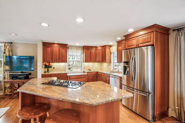 kitchen featuring a center island, stainless steel appliances, light stone counters, light hardwood / wood-style floors, and a kitchen bar