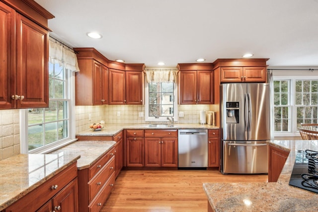 kitchen featuring light wood-type flooring, stainless steel appliances, light stone counters, and sink