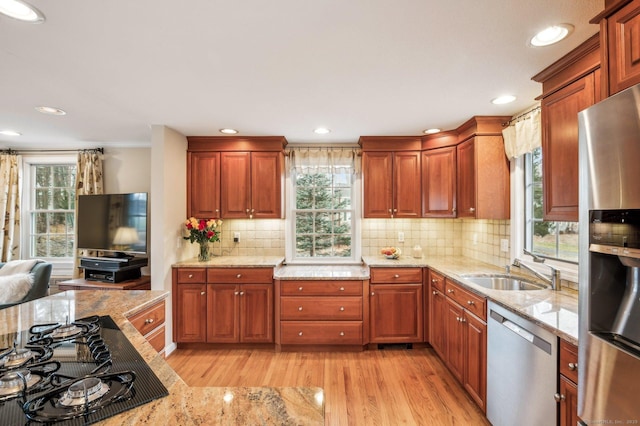 kitchen featuring decorative backsplash, appliances with stainless steel finishes, light stone counters, sink, and light hardwood / wood-style floors