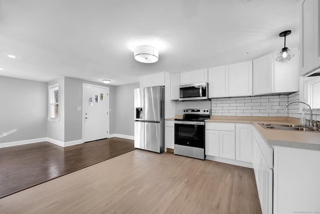 kitchen featuring pendant lighting, sink, light wood-type flooring, white cabinetry, and stainless steel appliances