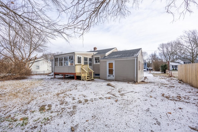 snow covered back of property featuring a sunroom