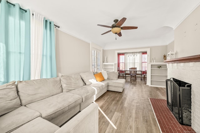 living room with ceiling fan, a fireplace, wood-type flooring, and ornamental molding