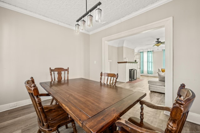 dining area featuring ceiling fan, a fireplace, crown molding, and hardwood / wood-style flooring