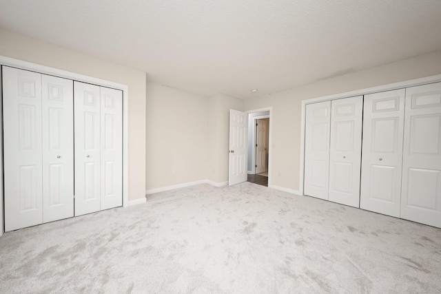 unfurnished bedroom featuring light carpet and multiple closets