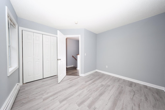 unfurnished bedroom with light hardwood / wood-style flooring, baseboard heating, and a closet