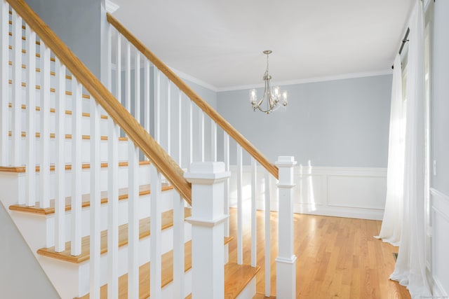 staircase featuring hardwood / wood-style flooring, crown molding, and a chandelier