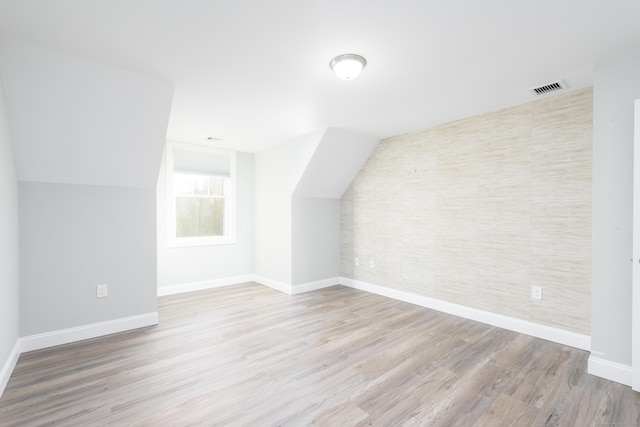 bonus room with light wood-type flooring and vaulted ceiling