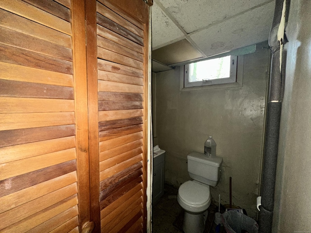 bathroom with wooden walls, toilet, and a drop ceiling