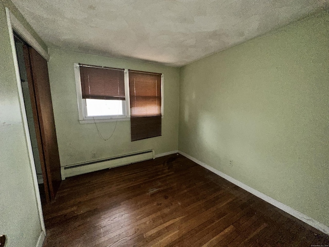 empty room featuring dark hardwood / wood-style flooring and a baseboard heating unit