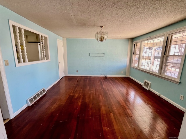 unfurnished dining area with brick wall, dark wood-type flooring, a textured ceiling, and a notable chandelier