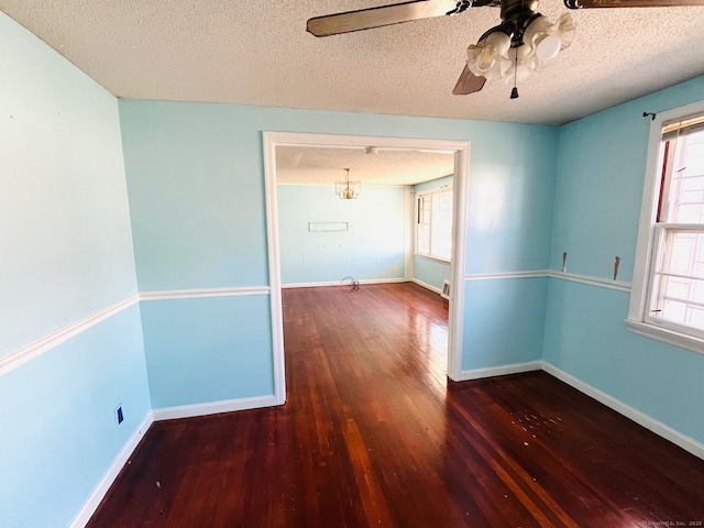 spare room with dark hardwood / wood-style flooring, ceiling fan with notable chandelier, and a textured ceiling