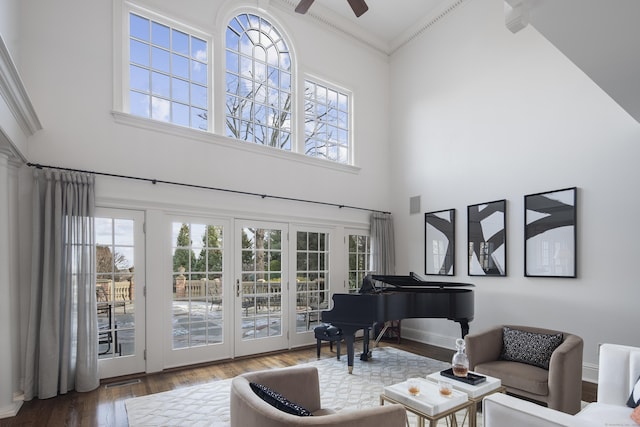 sitting room with ceiling fan, wood-type flooring, ornamental molding, and a towering ceiling