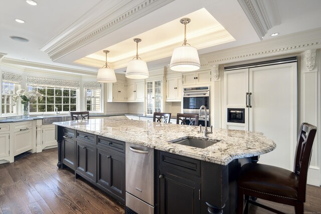 kitchen with sink, a kitchen island with sink, white cabinets, and pendant lighting