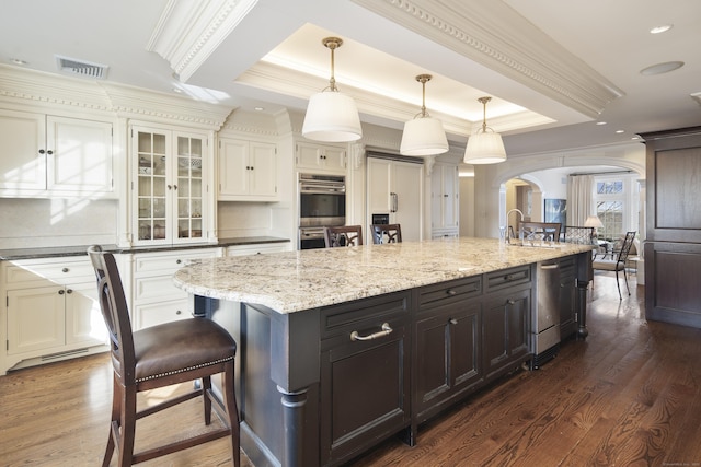 kitchen with hanging light fixtures, a raised ceiling, appliances with stainless steel finishes, ornamental molding, and a large island with sink