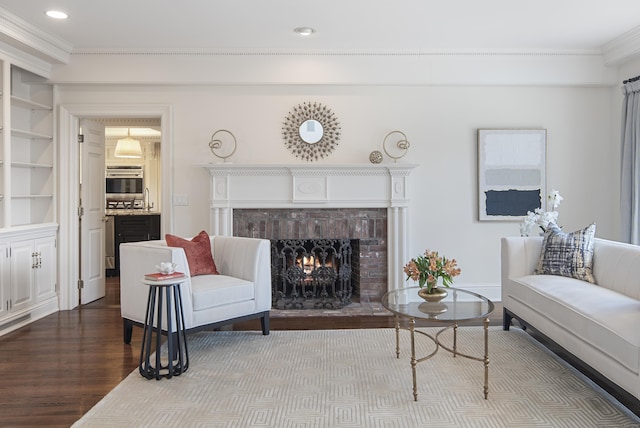 living room featuring a brick fireplace, built in shelves, crown molding, and hardwood / wood-style floors