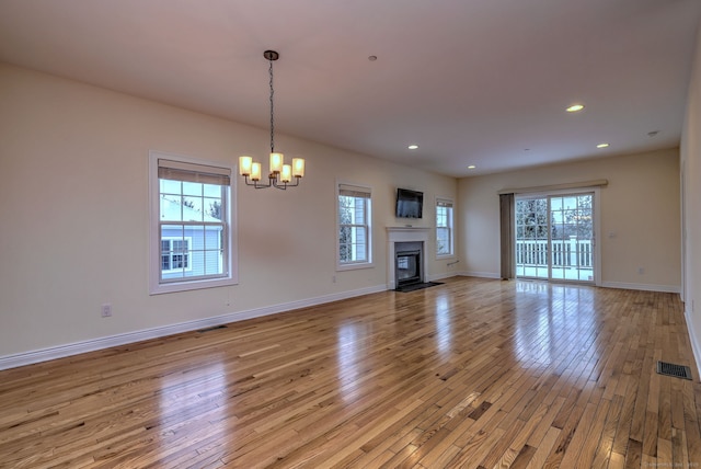 unfurnished living room with a notable chandelier, a wealth of natural light, and light hardwood / wood-style flooring