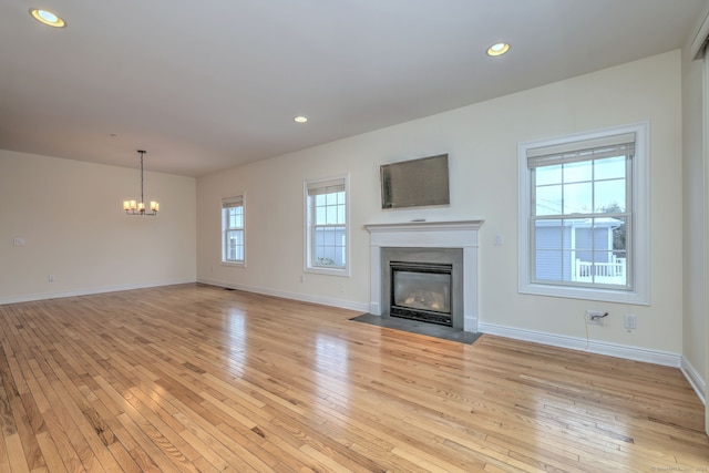 unfurnished living room featuring light hardwood / wood-style floors, an inviting chandelier, and a healthy amount of sunlight