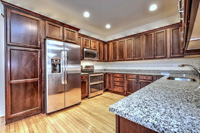 kitchen featuring appliances with stainless steel finishes, light wood-type flooring, light stone counters, dark brown cabinetry, and sink