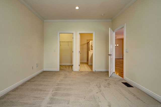 unfurnished bedroom featuring light carpet, ensuite bathroom, a spacious closet, and ornamental molding